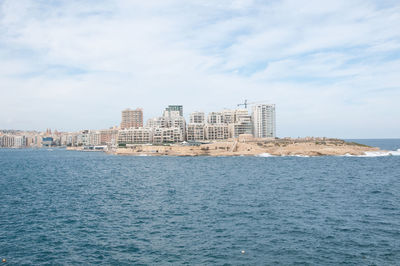 Sea by buildings against sky in city