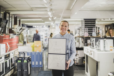 Portrait of smiling mature female owner with boxes standing in electronics store