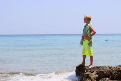 Little boy standing at beach against sky