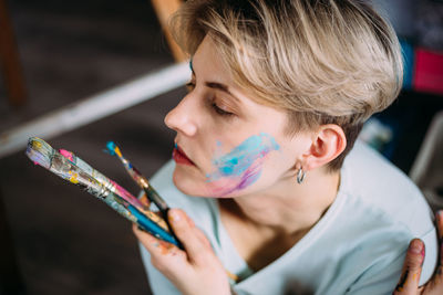 Creative portrait of beautiful young woman artist in studio with brushes.