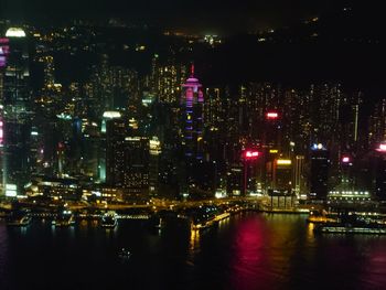 Illuminated buildings by river against sky at night