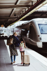 Full length of mother and daughter with luggage walking on platform at train station