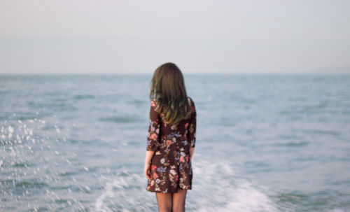 Rear view of woman standing at beach against clear sky