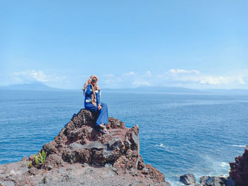 Young woman on rock by sea against sky
