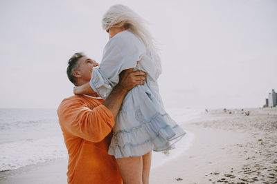 Side view of man lifting woman at beach