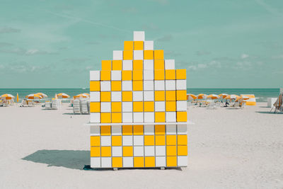 Stack of yellow deck chairs on beach against sky