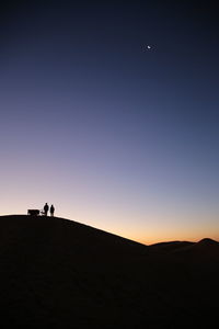 Silhouette people on land against sky during sunset