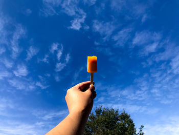 Cropped hand holding food against blue sky