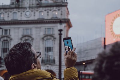 Rear view of woman photographing with mobile phone in city