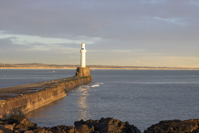 Lighthouse by sea against sky during sunset