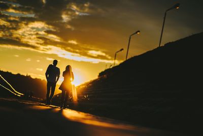 Full length of silhouette friends walking on street against sky during sunset
