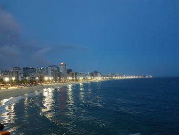 Illuminated city by sea against sky at night