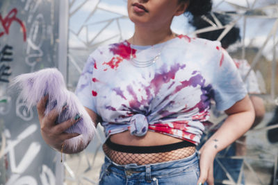 Midsection of young woman holding mobile phone against mosaic wall