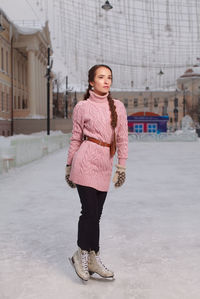 Young pretty woman dressed pink sweatshirt standing on ice in skates, outdoor ice-scating rink