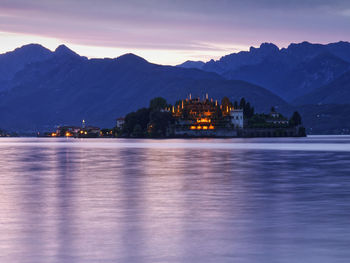 Illuminated buildings by mountains against sky at sunset