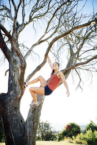 Happy sporty woman hanging from branch against clear sky