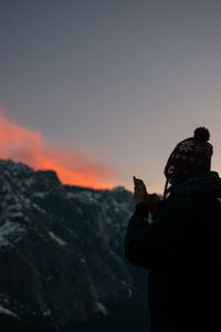 Side view of man photographing against sky during sunset