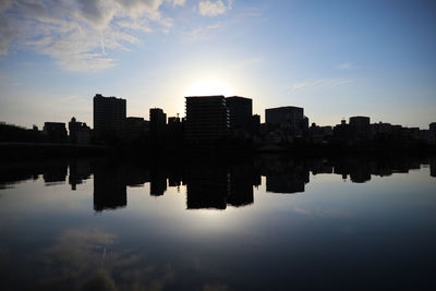 Reflection of silhouette buildings in lake against sky during sunset