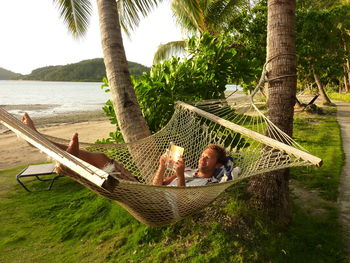 Man reading book while relaxing in hammock at park