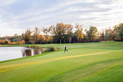 Scenic view of golf course by lake against sky