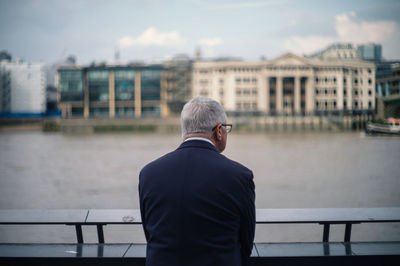 Rear view of man standing by railing against river