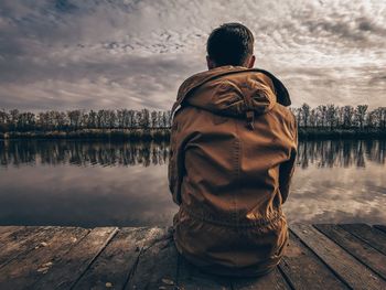 Rear view of man standing on pier over lake against sky