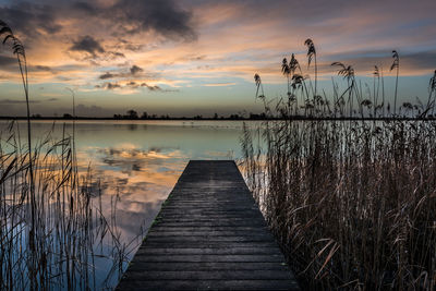 Jetty in lake against sunset sky