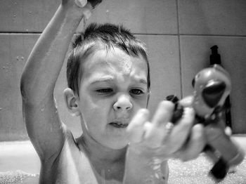 Shirtless boy holding toys while bathing in bathroom