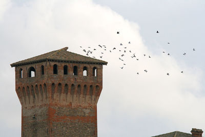 Low angle view of seagulls flying over old building against sky