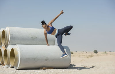 Woman jumping over pipe against sky