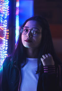 Portrait of young woman standing against illuminated ride