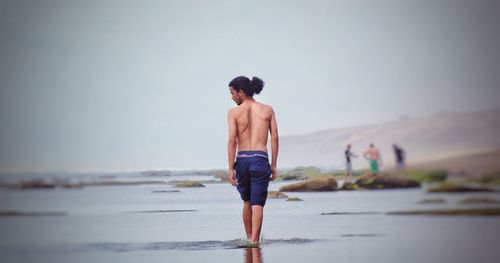 Rear view of shirtless man walking on beach against clear sky