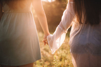 Midsection of lesbian couple holding hands while standing in forest