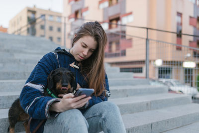 Young adult woman looking her smartphone sit next to her dachshund dog