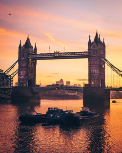 Boats moored on river by tower bridge against sky during sunset