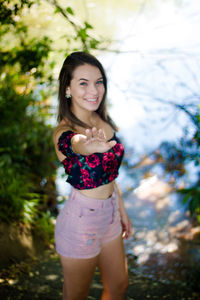 High angle portrait of smiling teenage girl with hand raised standing against lake