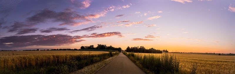 Empty road amidst field against sky during sunset