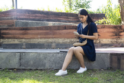 Full length portrait of young woman sitting on mobile phone