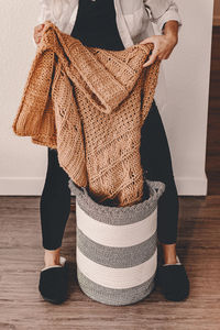 Low section of woman putting clothes in container on floor at home