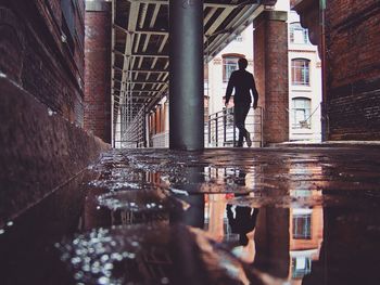 Rear view full length of man reflecting on puddle at corridor in building