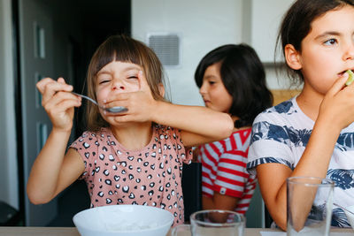 Three girls eating lunch at home at white table with father cooking in background