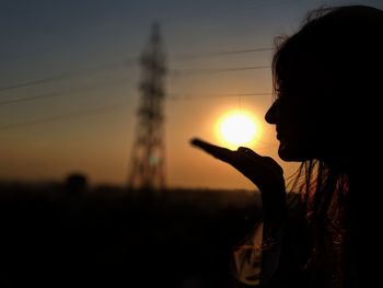 Optical illusion of silhouette woman holding sun against sky during sunset