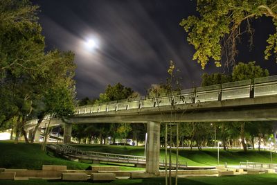 Bridge over road against trees at night
