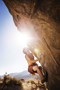 Shirtless man climbing rock against clear sky on sunny day