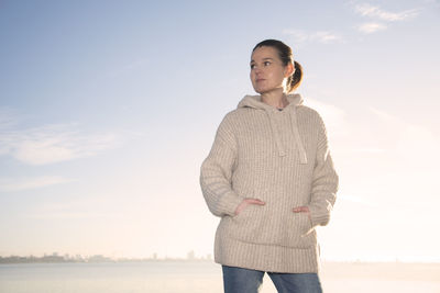 Woman wearing beige sweater, walking by the sea enjoying the sun.