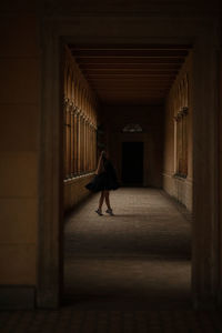 Full length of young woman standing in dark corridor