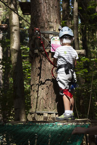 Rear view of girl climbing on tree trunk in forest