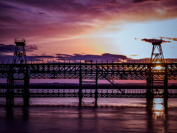 Silhouette bridge over sea against sky during sunset