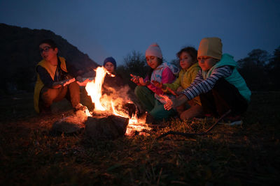 Kids sitting by bonfire against sky