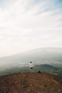 Rear view of man standing on mountain against sky